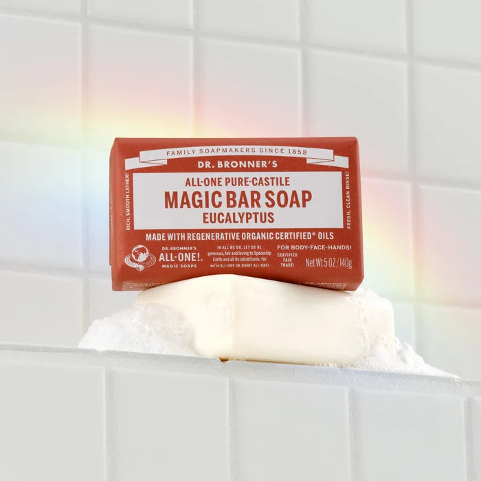 Bar of Dr. Bronners Eucalyptus Magic Bar Soap rests on white tiles with suds and a subtle rainbow effect. Dr. Bronners Magic Bar Soap Eucalyptus, Certified Organic, Fair Trade, Net Wt 5 oz140g [5 oz]