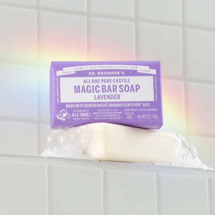 Bar soap labeled Dr. Bronners Magic Bar Soap Lavender rests on a soap dish with a rainbow reflection on white tiled wall. Promotes organic, vegan, and eco friendly properties [5 oz]