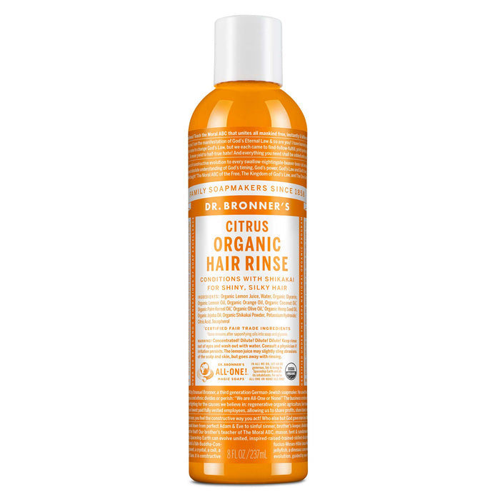 A bottle of Dr. Bronners Citrus Organic Hair Rinse stands upright. The orange bottle features detailed text about its conditioning benefits with shikakai for shiny, silky hair. Label promotes fair trade and organic certification [8 oz]